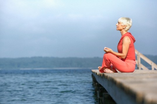 Senior woman practicing yoga on jetty